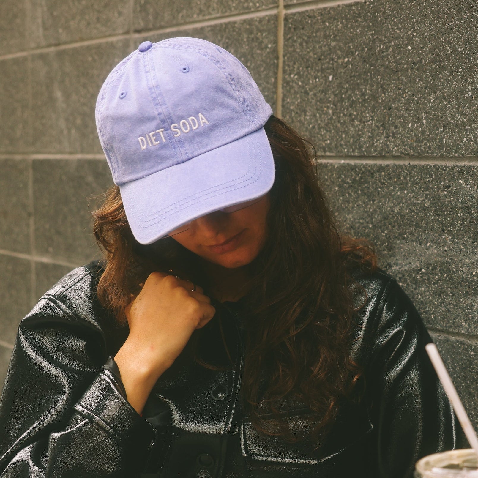 Two people standing against a gray wall, one holding a drink.