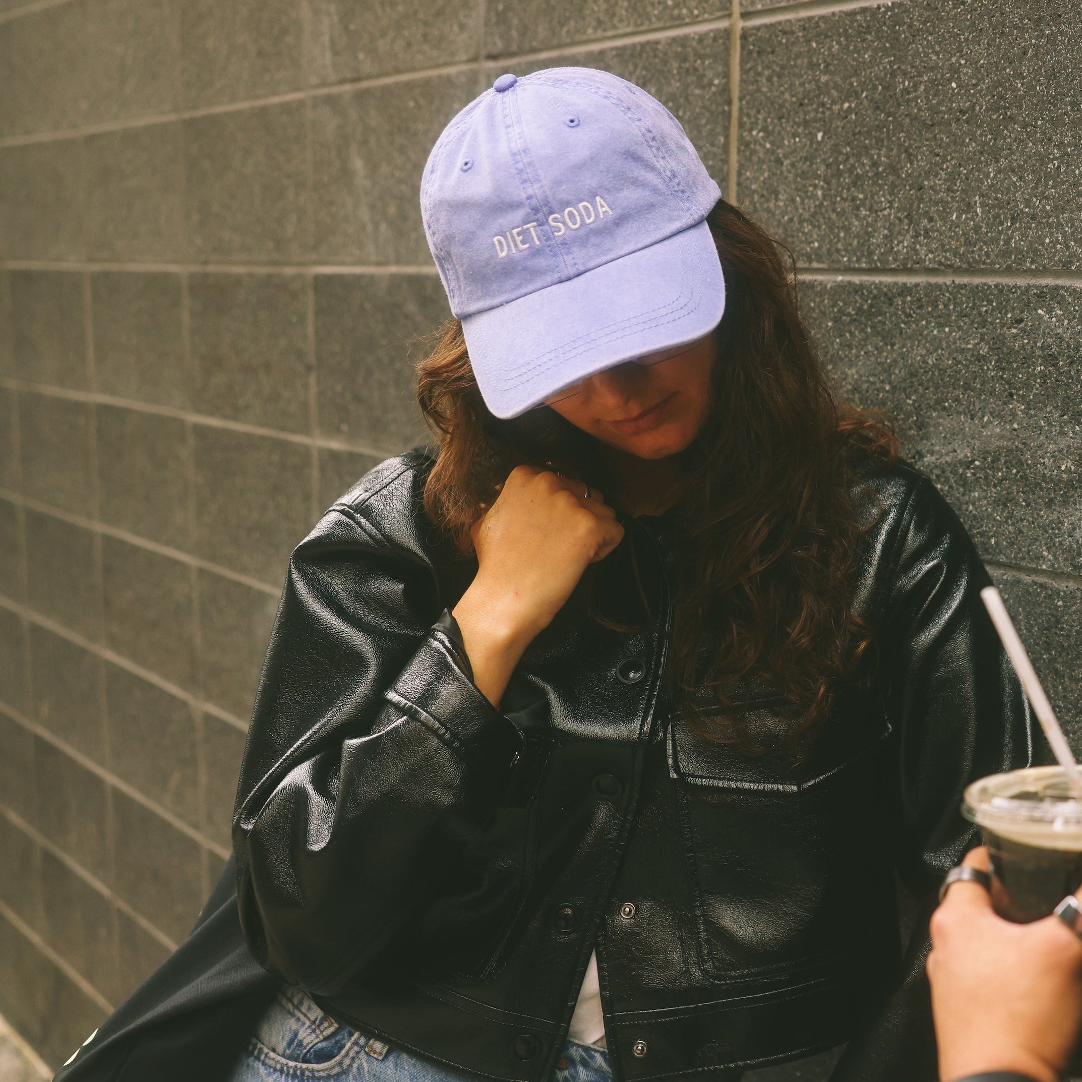 Two people standing against a gray wall, one holding a drink.