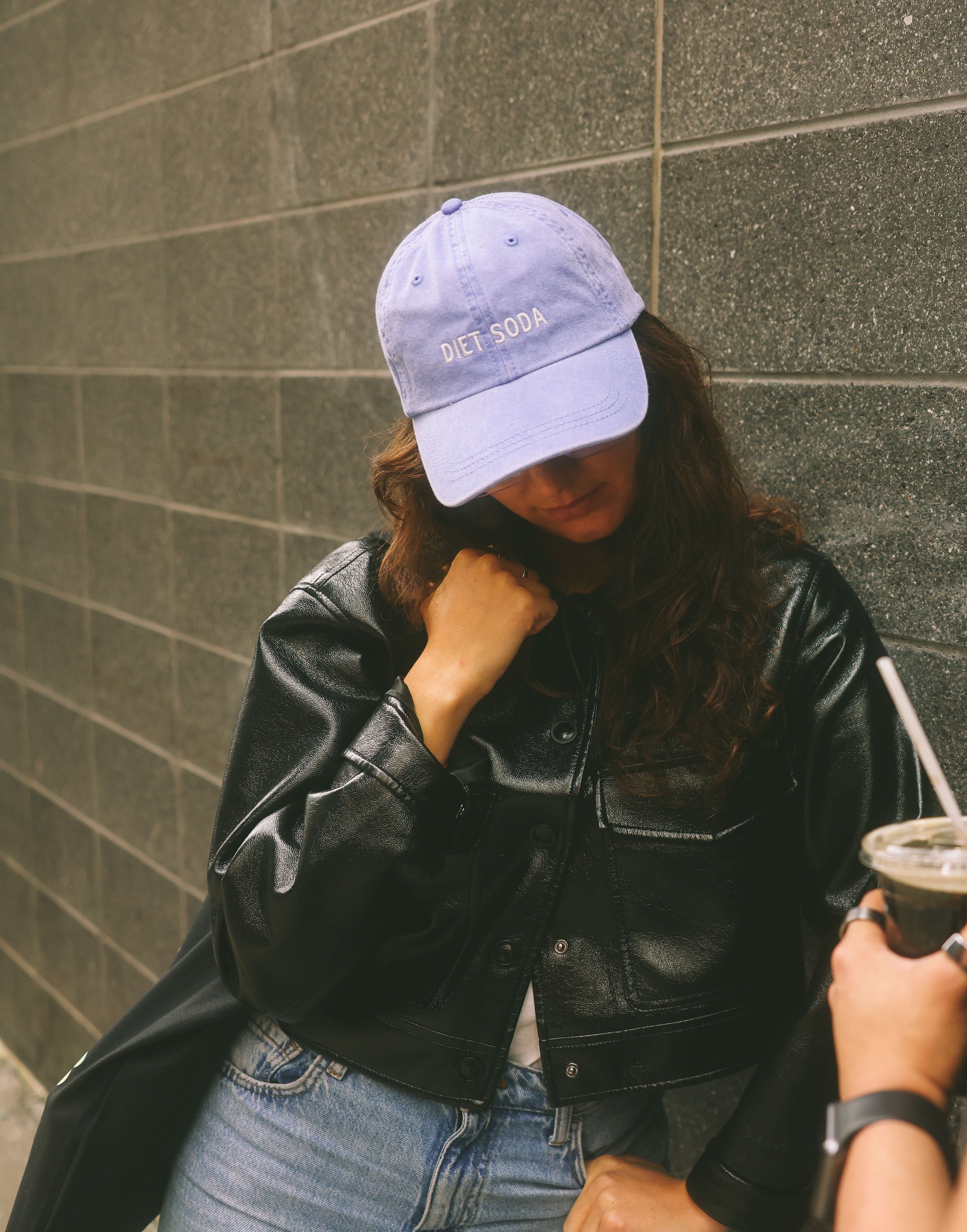 Two people standing against a gray wall, one holding a drink.