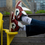 A person wearing jeans rests their feet on a yellow chair, showcasing brown Nike sneakers and white socks that feature a black circle with the words "Inside Out."