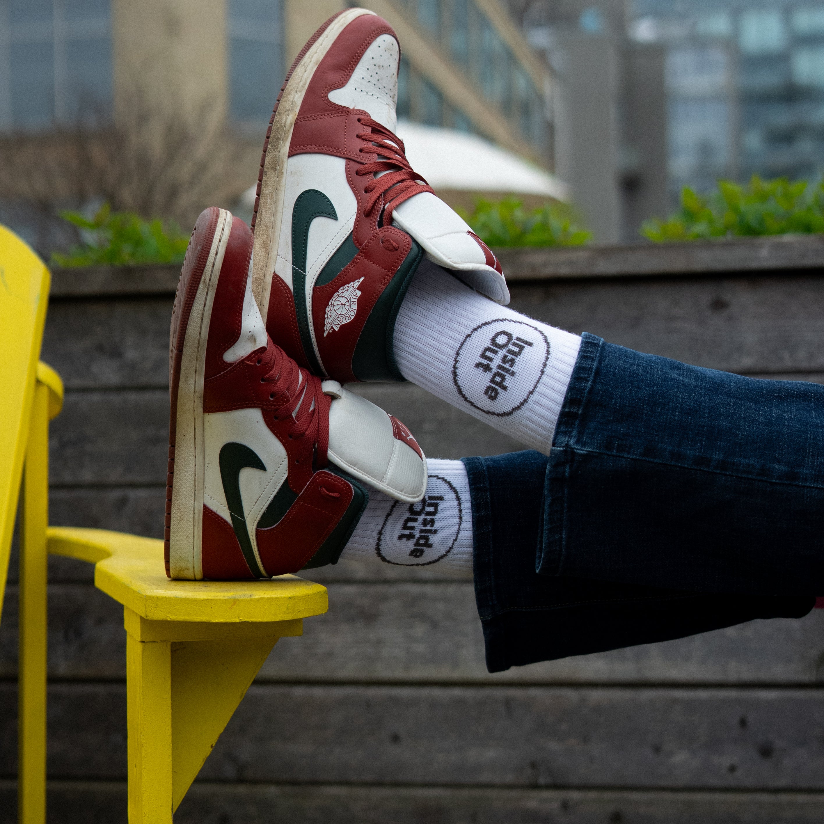 A person wearing jeans rests their feet on a yellow chair, showcasing brown Nike sneakers and white socks that feature a black circle with the words "Inside Out."