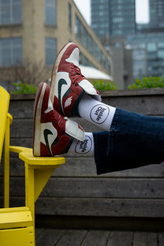 A person wearing jeans rests their feet on a yellow chair, showcasing brown Nike sneakers and white socks that feature a black circle with the words "Inside Out."