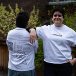 Two people lean against each other on an outdoor patio wearing matching white graphic t-shirts from "Inside Out," with one person showing the minimalist front text logo and the other showcasing a detailed back design filled with text and diagrams.