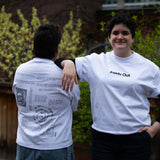 Two people lean against each other on an outdoor patio wearing matching white graphic t-shirts from "Inside Out," with one person showing the minimalist front text logo and the other showcasing a detailed back design filled with text and diagrams.