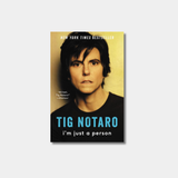 Sepia toned close-up portrait of person looking directly at the camera with a deadpan expression. The title "TIG NOTARO" is printed in large, bold blue capital letters across their chest, with the subtitle in smaller white lowercase text below it.