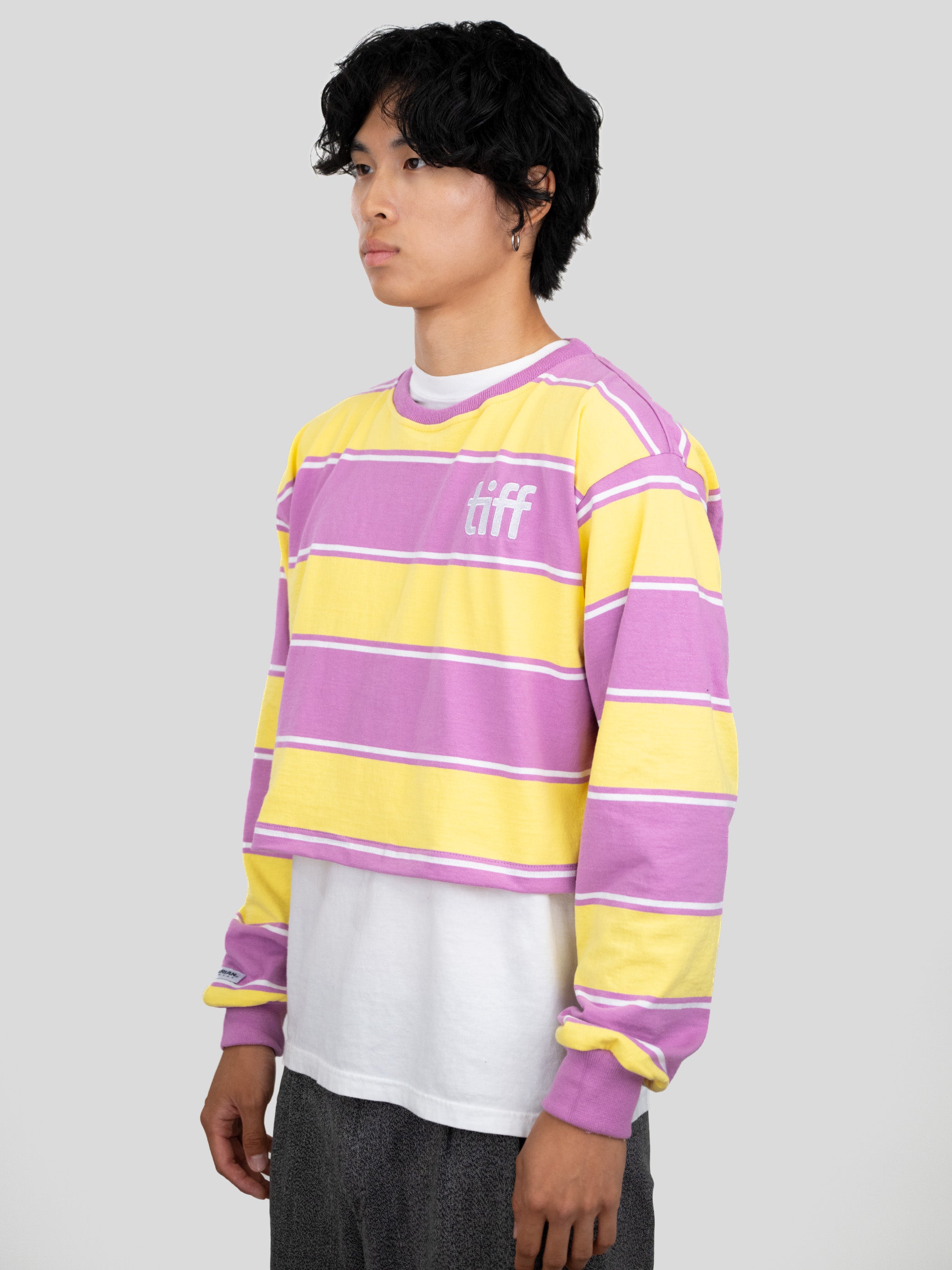 A model wears a long-sleeved cropped shirt featuring yellow, purple, and white stripes with the "TIFF" logo printed on the chest.