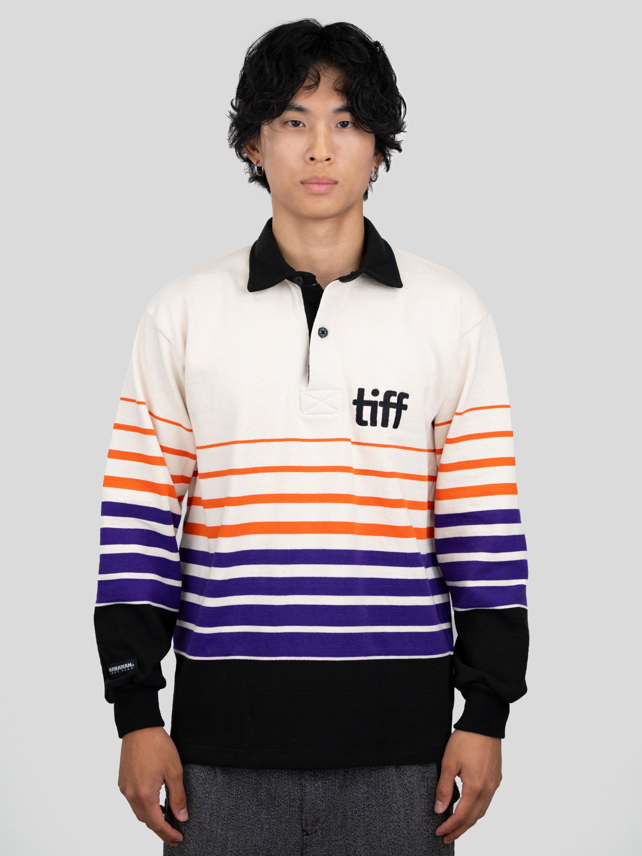 A model wears a long-sleeved, collared rugby shirt featuring orange, purple, and black stripes with the "TIFF" logo printed on the left chest.