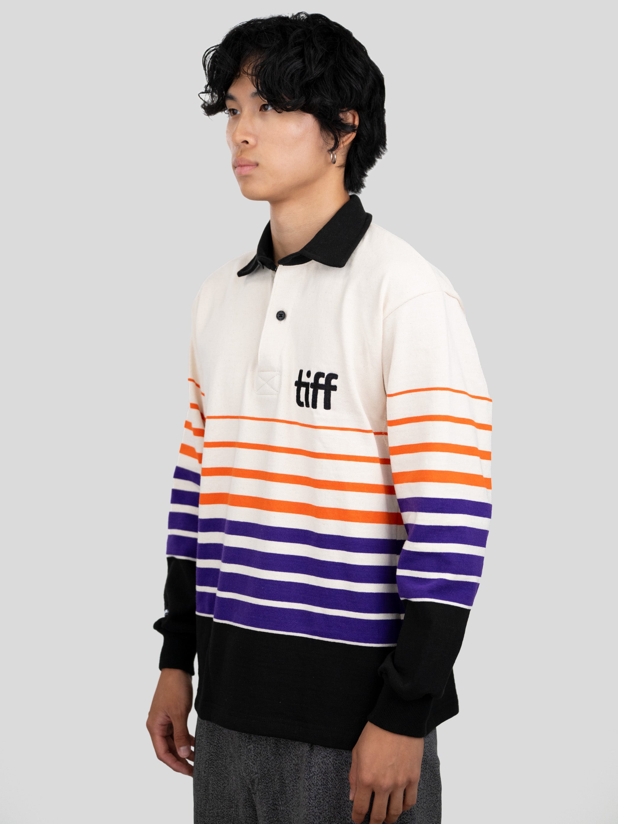 A model wears a long-sleeved, collared rugby shirt featuring orange, purple, and black stripes with the "TIFF" logo printed on the left chest.