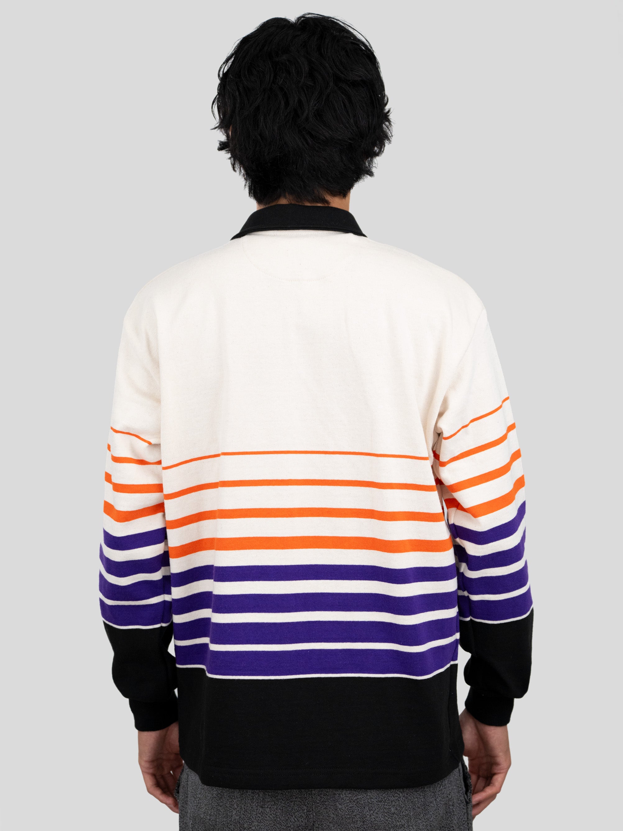 Back of model wearing a long-sleeved, collared rugby shirt featuring orange, purple, and black stripes.