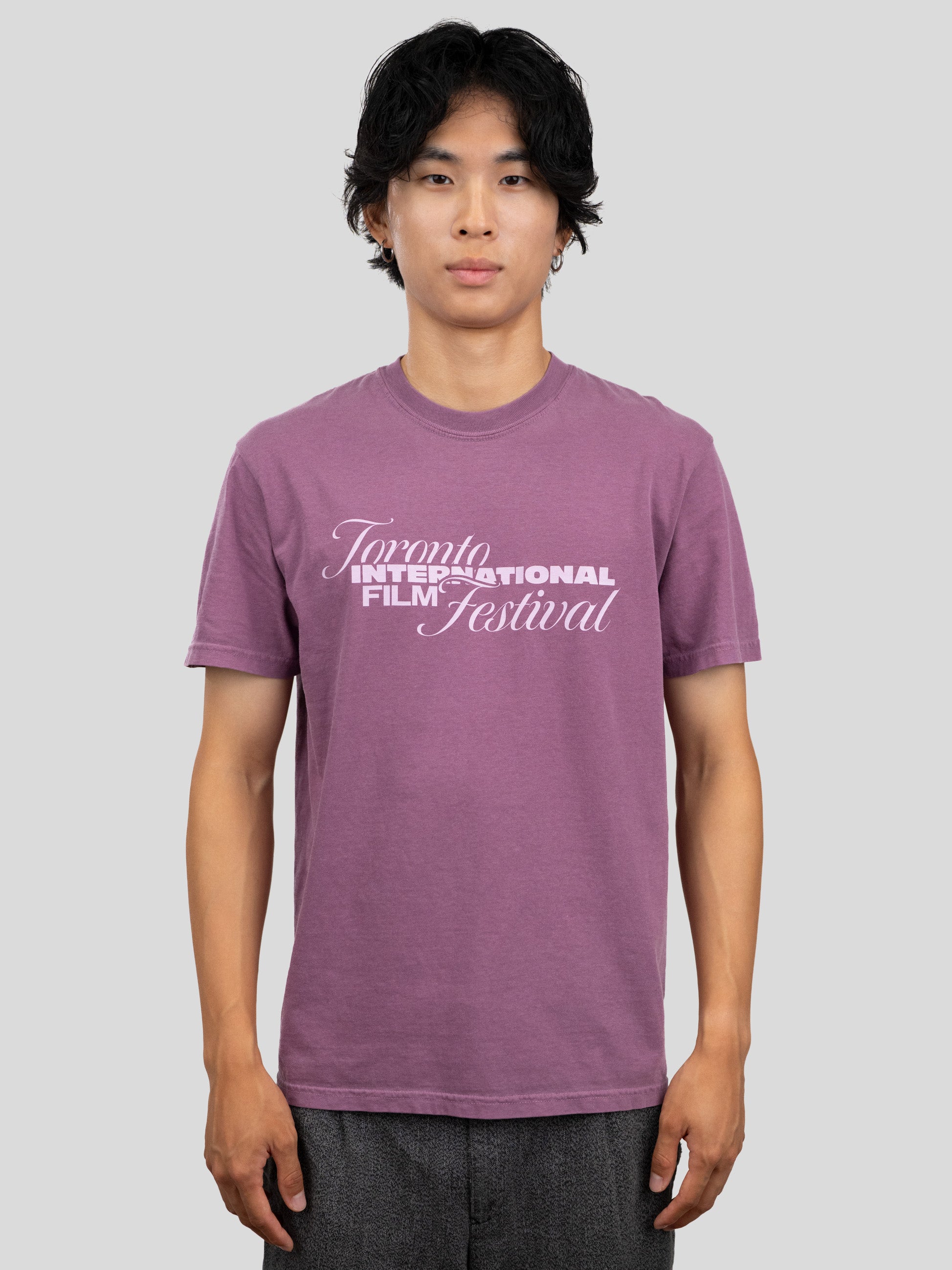 A man wearing a heathered purple t-shirt with a white graphic print that reads 'Toronto International Film Festival' on the chest, standing against a solid gray background.