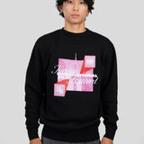 A man wearing a black crewneck sweatshirt with a pink and white graphic print for the Toronto International Film Festival, paired with gray trousers, against a solid light gray background.