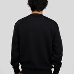 A man viewed from behind wearing a plain black long-sleeve crewneck sweater and gray trousers, set against a solid light gray background.