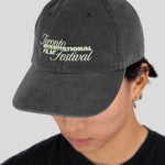 A person wearing a dark gray washed baseball cap with 'Toronto International Film Festival' embroidered in light green and white on the front, against a light gray background.