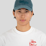 A young man wearing a dusty blue baseball cap with 'Toronto International Film Festival' embroidered on the front, paired with a white t-shirt featuring a red graphic on the chest, set against a plain light gray background.