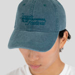 A person wearing a blue denim baseball cap with 'Toronto International Film Festival' embroidered in dark blue on the front, photographed against a light gray background.