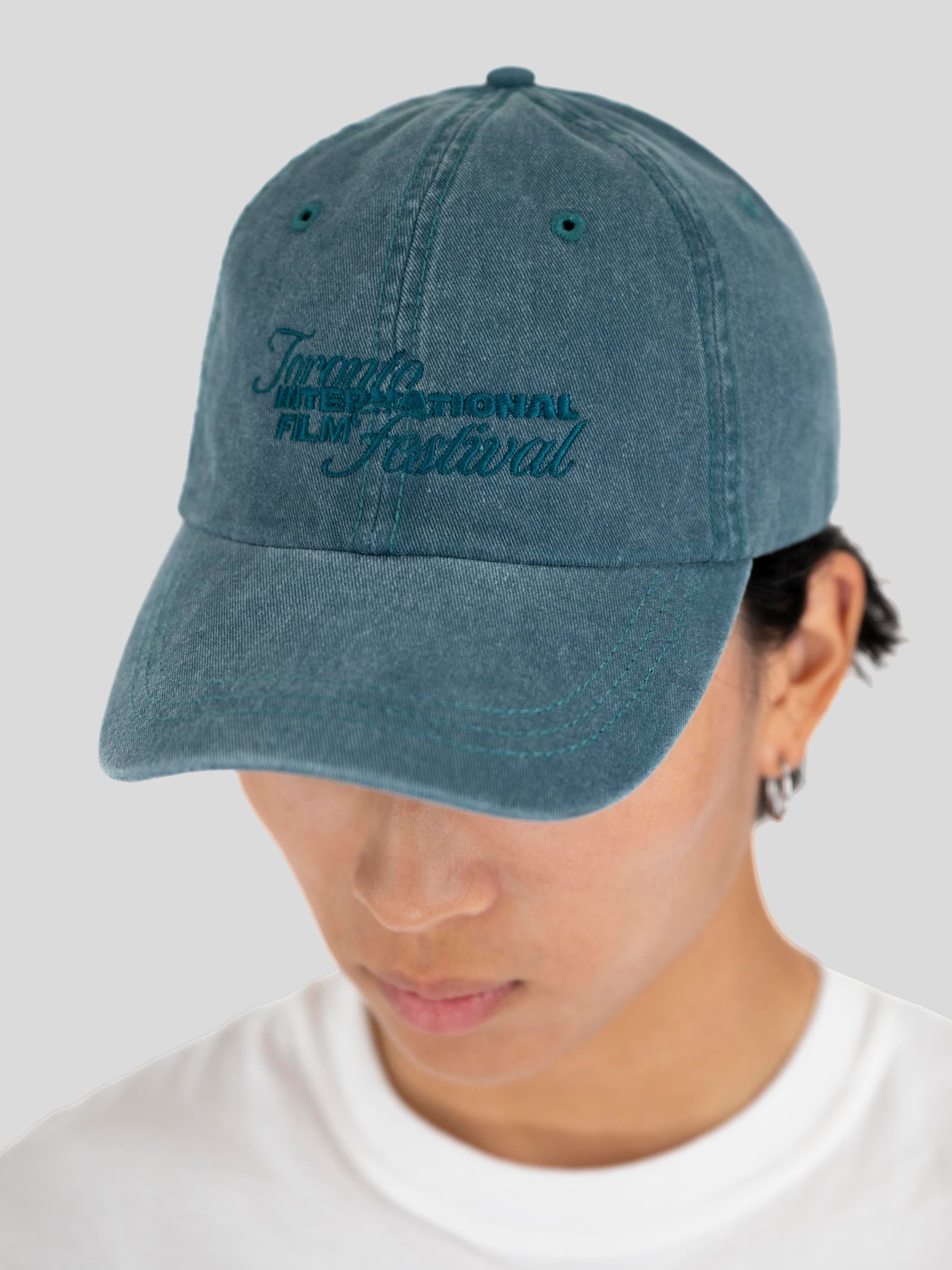 A person wearing a blue denim baseball cap with 'Toronto International Film Festival' embroidered in dark blue on the front, photographed against a light gray background.