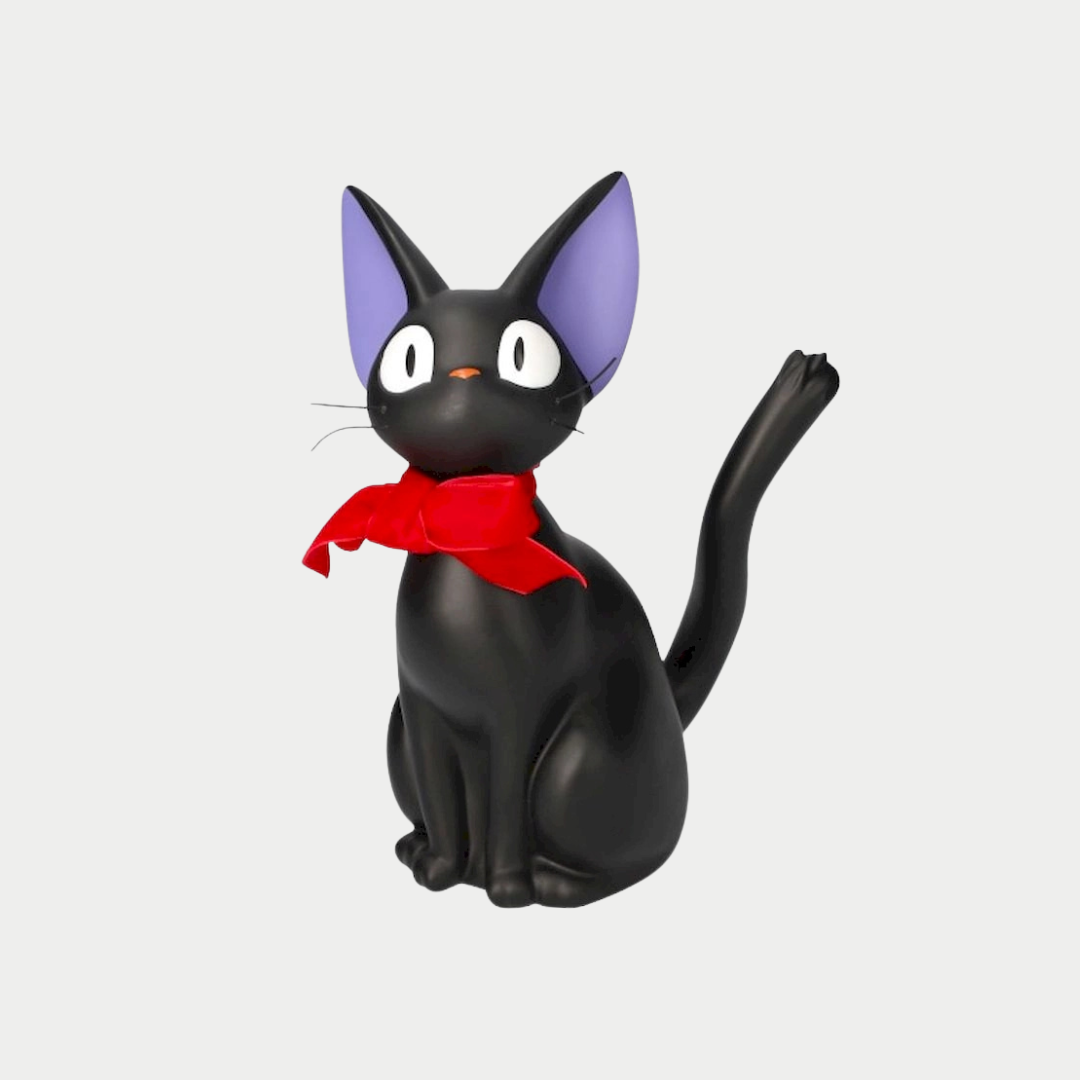 A black cat figurine representing Jiji from Kiki's Delivery Service sits upright with large eyes, purple inner ears, and a prominent red bow tied around its neck.
