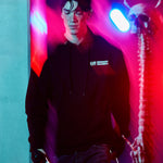 A person wearing a black "TIFF Midnight Madness" hoodie and beanie walks through a blurred, neon-lit space featuring red and purple lights and a skeletal figure.