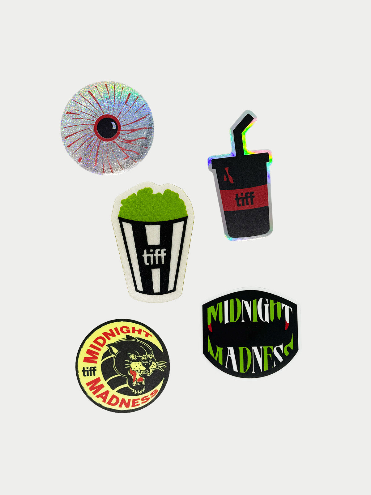 Group of five stickers with one glitter bloodshot eyeball, halographic black and red soda cup with straw, textured green popcorn with black and white striped bucket, green and white midnight madness logo with fangs, and round sticker with moon and panther graphic. 