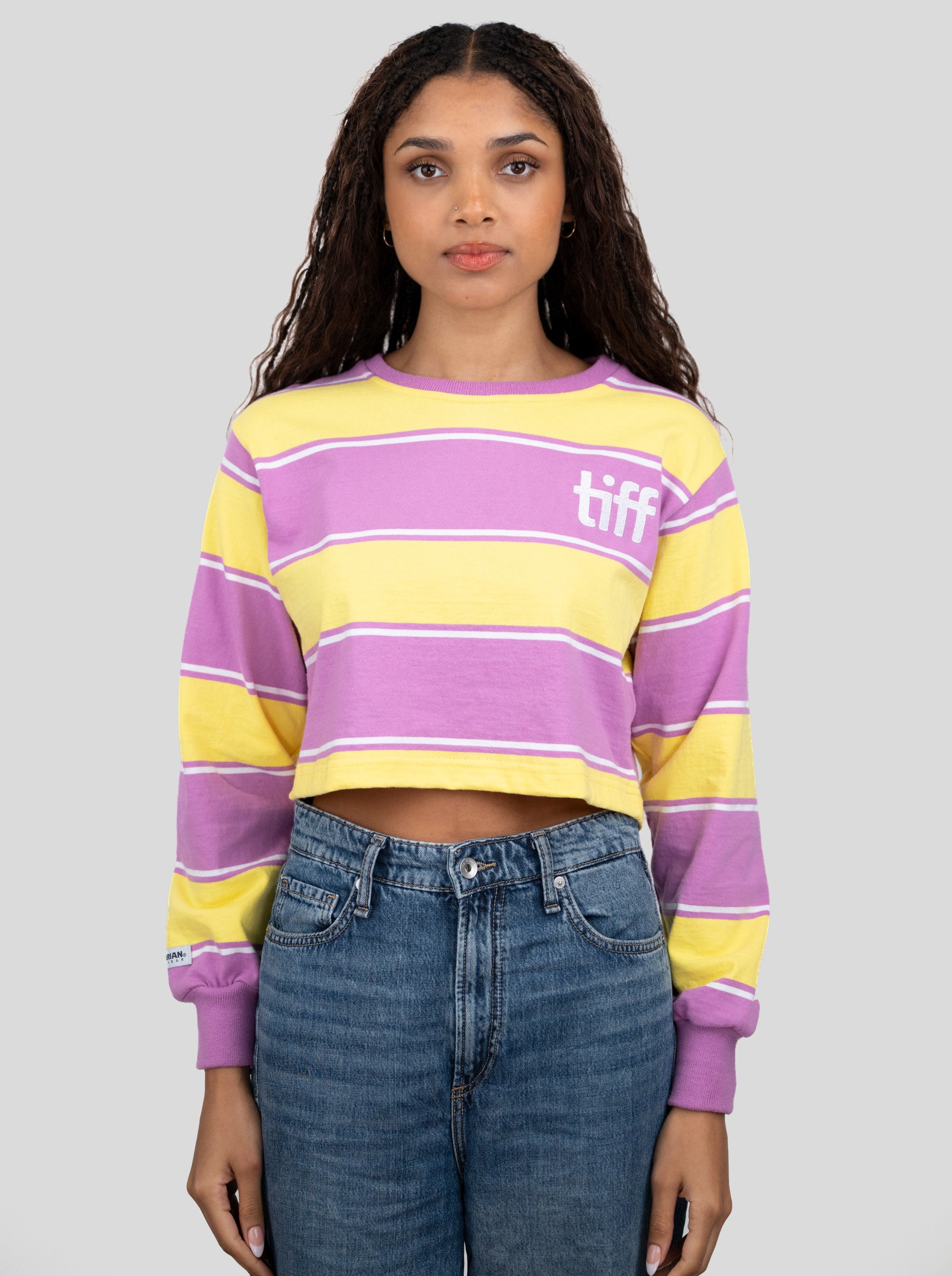 A model wears a long-sleeved cropped shirt featuring yellow, purple, and white stripes with the "TIFF" logo printed on the chest.