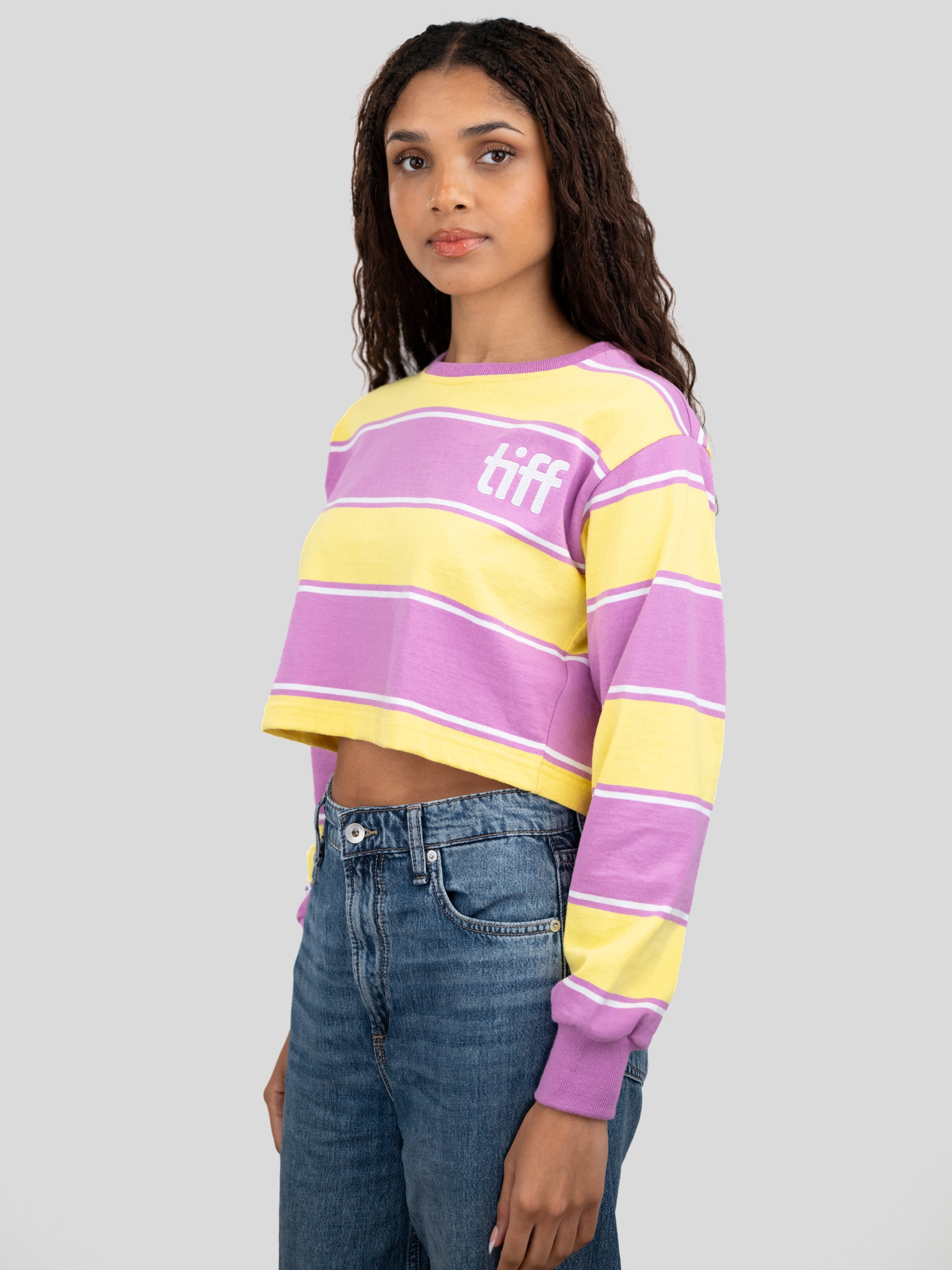 A model wears a long-sleeved cropped shirt featuring yellow, purple, and white stripes with the "TIFF" logo printed on the chest.