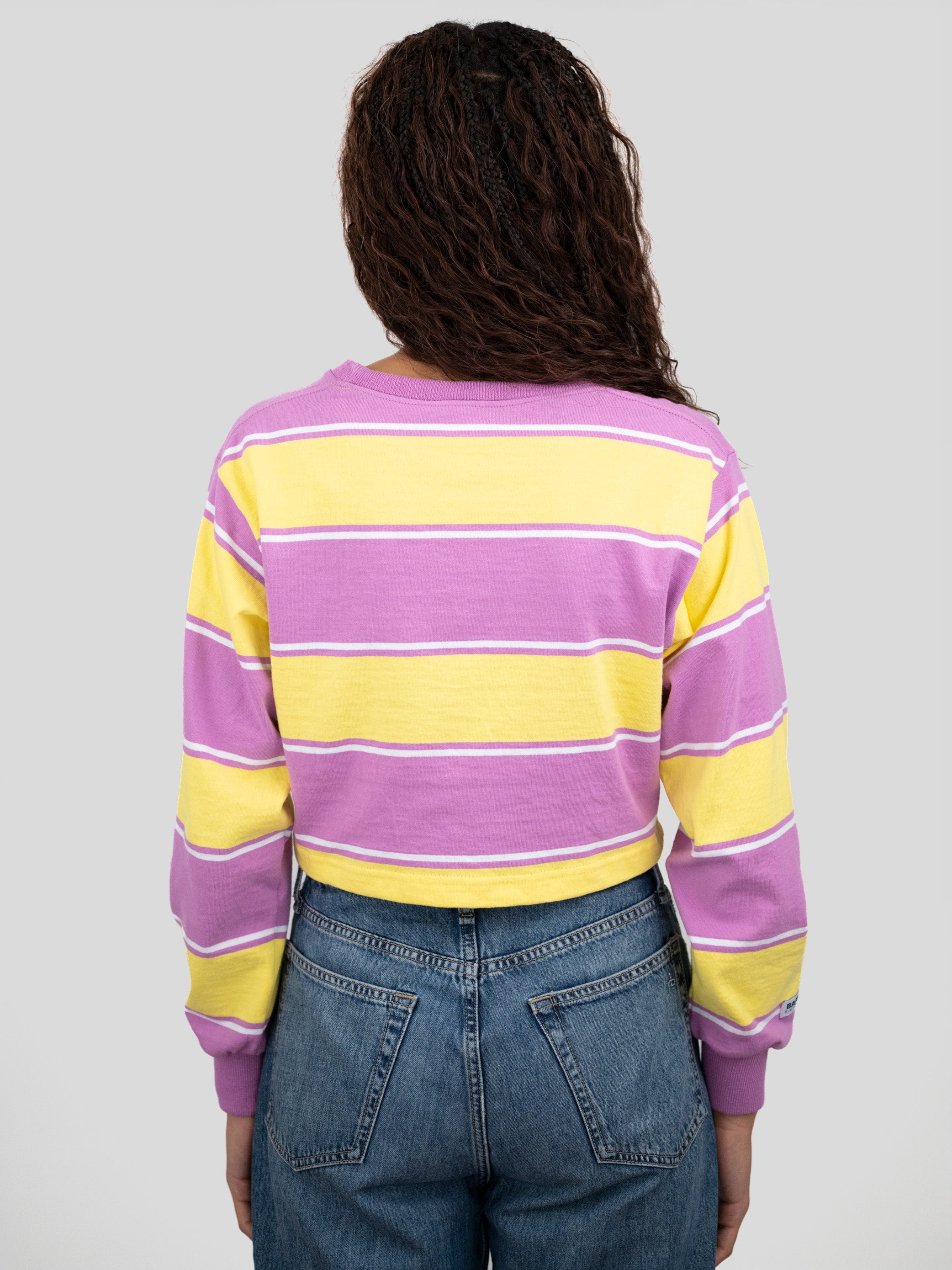 Back of model wearing a long-sleeved cropped shirt featuring yellow, purple, and white stripes.