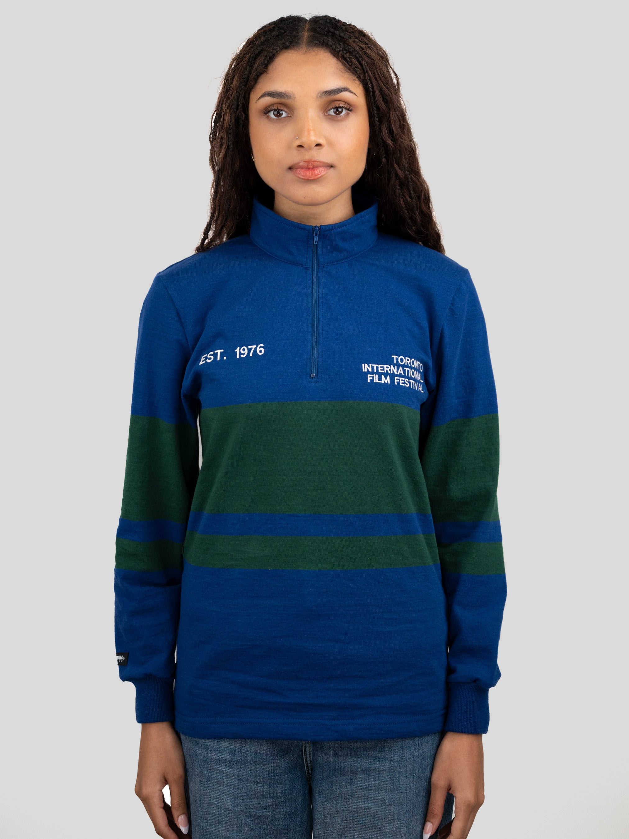 A model wears a blue and dark green quarter-zip pullover featuring "EST. 1976" and "TORONTO INTERNATIONAL FILM FESTIVAL" printed on the chest.
