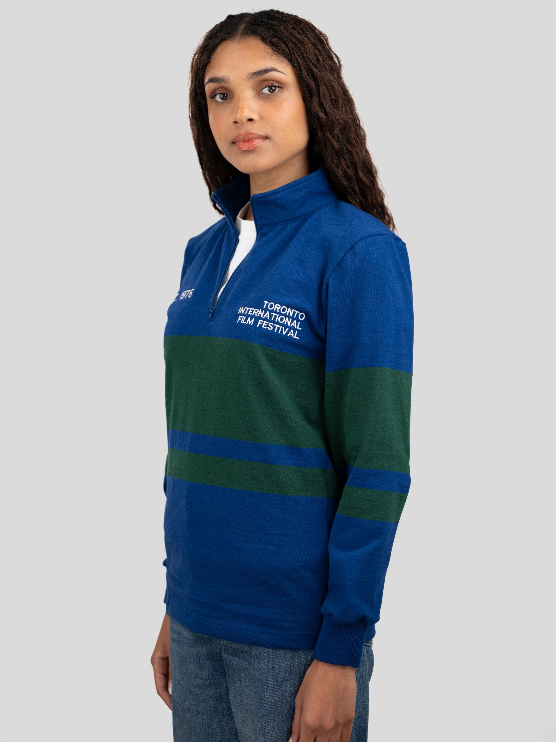 A model wears a blue and dark green quarter-zip pullover featuring "EST. 1976" and "TORONTO INTERNATIONAL FILM FESTIVAL" printed on the chest.