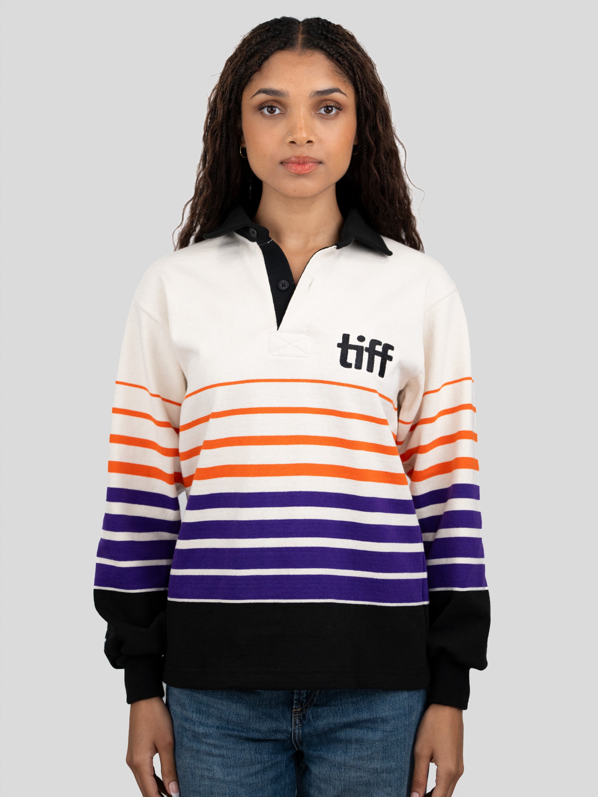 A model wears a long-sleeved, collared rugby shirt featuring orange, purple, and black stripes with the "TIFF" logo printed on the left chest.