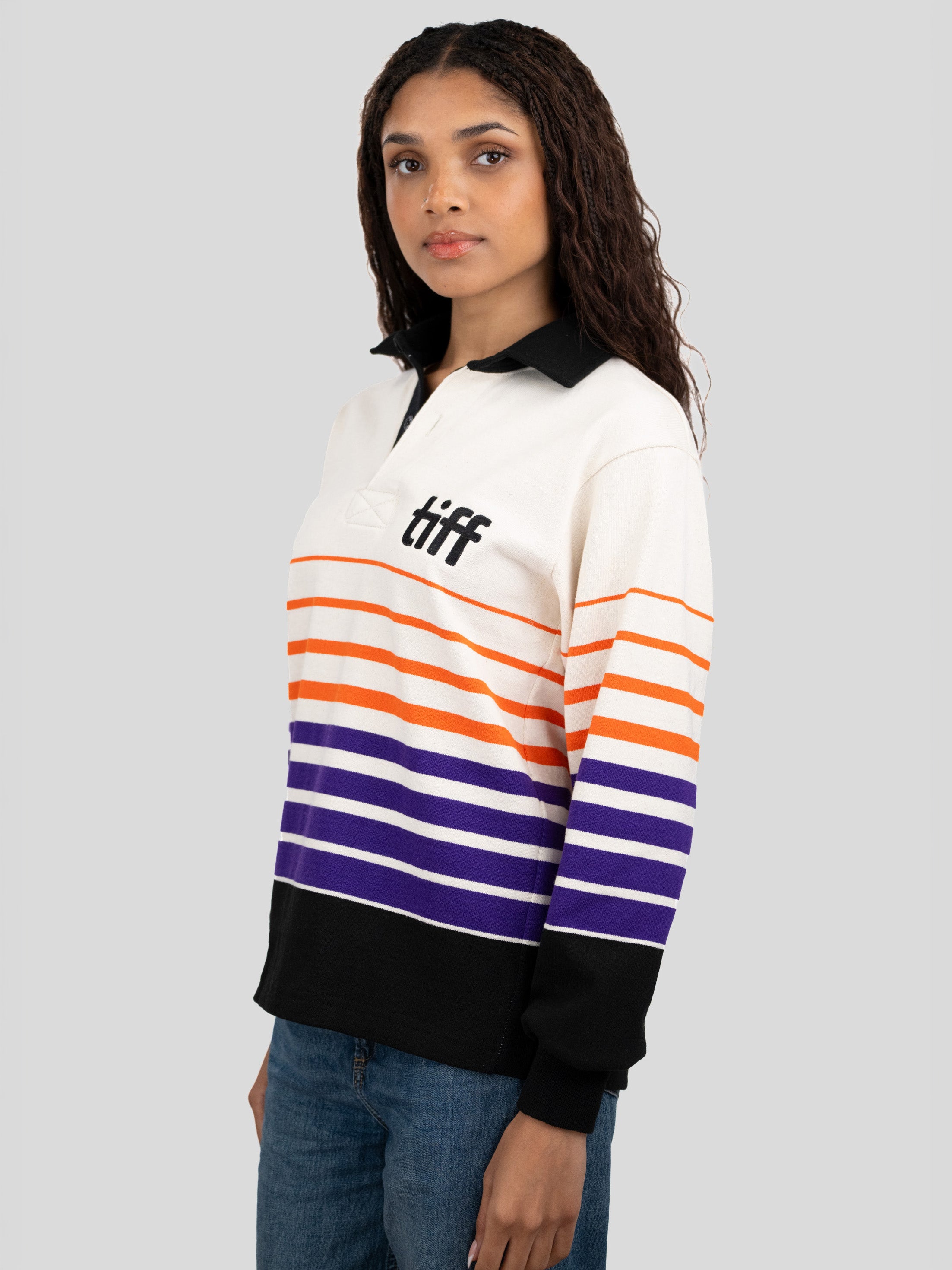A model wears a long-sleeved, collared rugby shirt featuring orange, purple, and black stripes with the "TIFF" logo printed on the left chest.