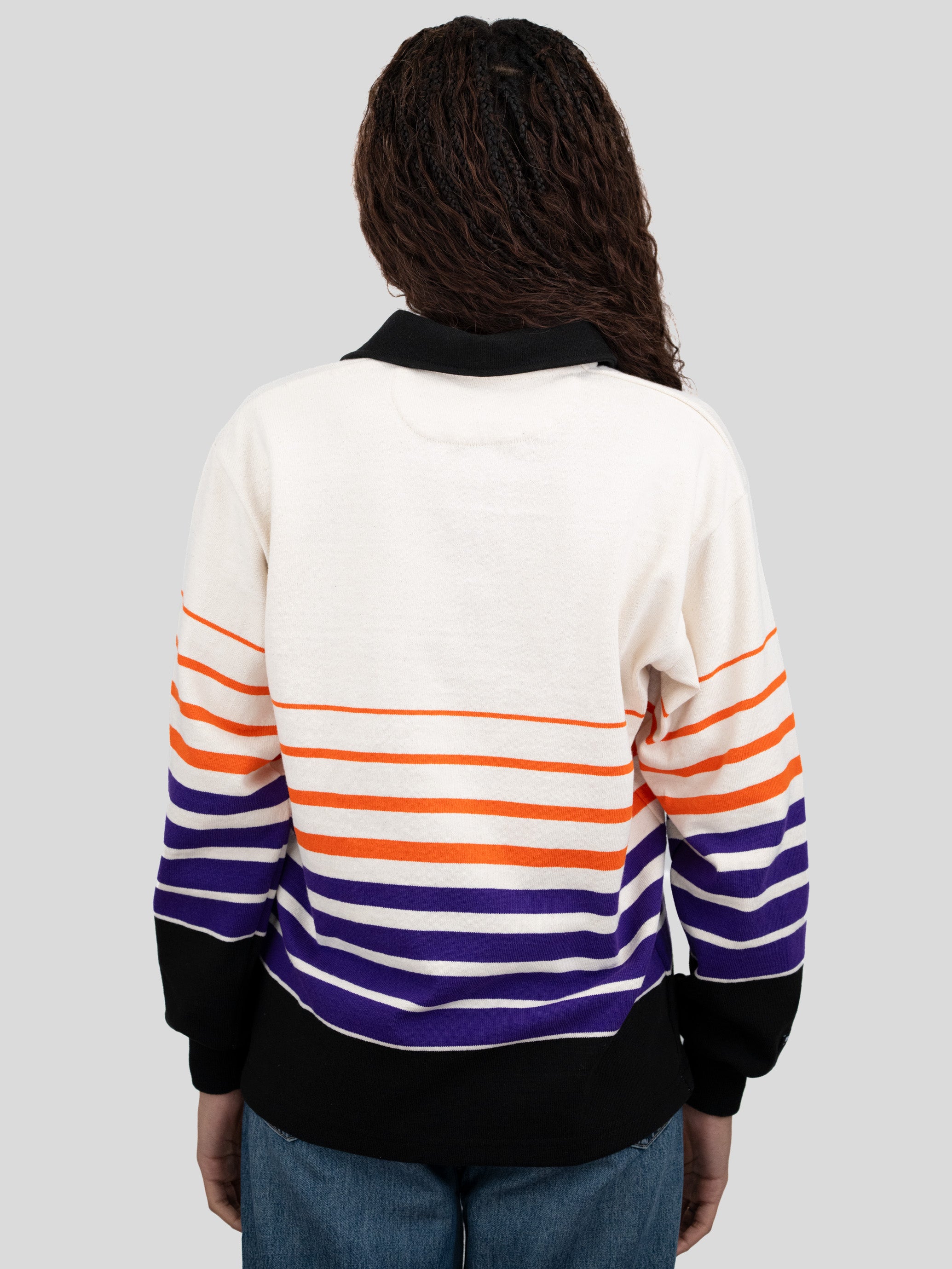Back of model wearing a long-sleeved, collared rugby shirt featuring orange, purple, and black stripes.