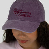 A person wearing a washed purple baseball cap with embroidered text reading 'Toronto International Film Festival' in dark red, shown against a light gray background.