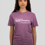 A woman wearing a purple short-sleeve crewneck t-shirt with 'Toronto International Film Festival' printed in white across the chest, paired with blue jeans, set against a solid light gray background.