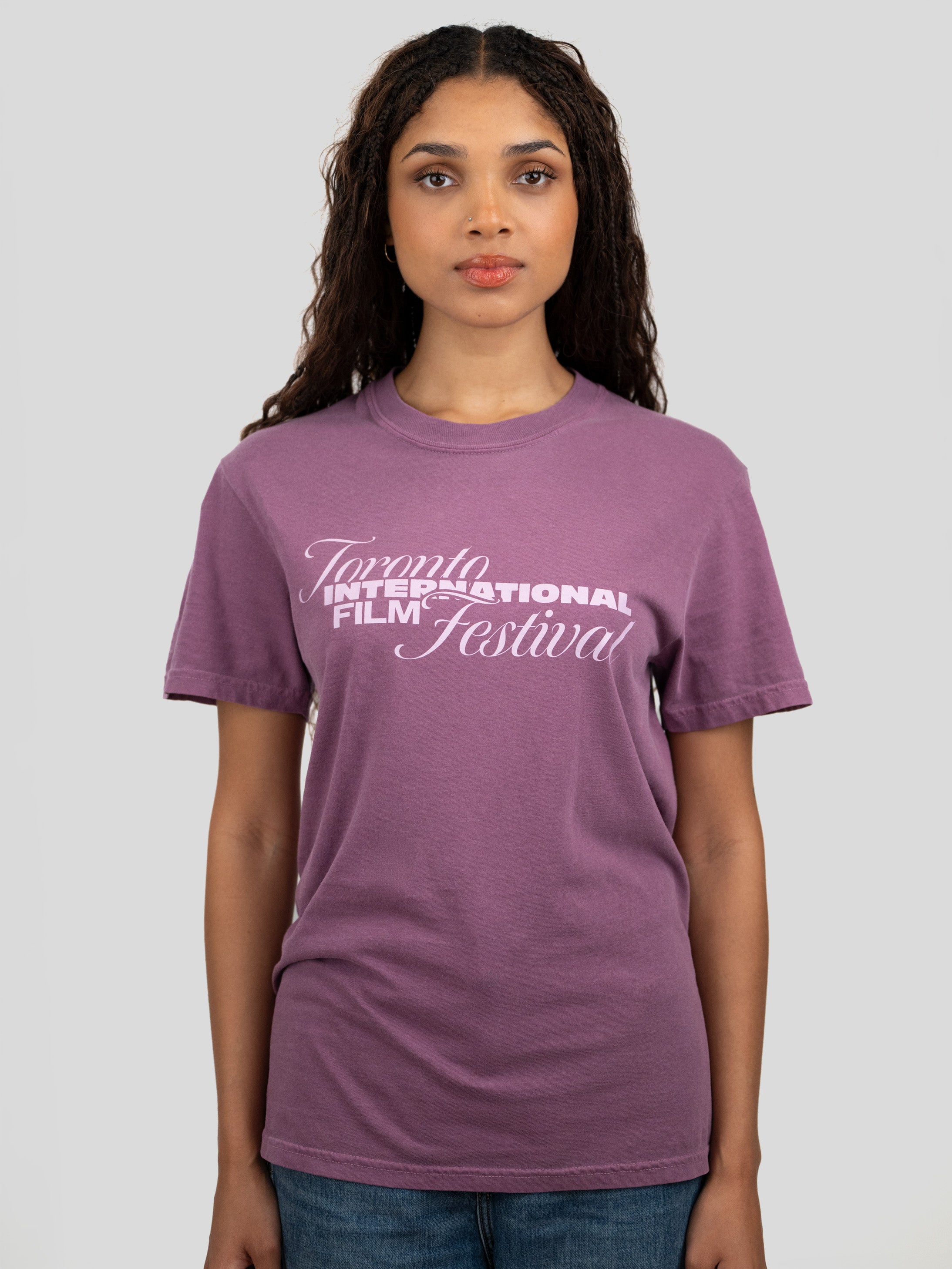 A woman wearing a purple short-sleeve crewneck t-shirt with 'Toronto International Film Festival' printed in white across the chest, paired with blue jeans, set against a solid light gray background.