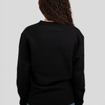 A person viewed from the back wearing a black long-sleeve crewneck sweater and blue jeans against a light gray studio background.