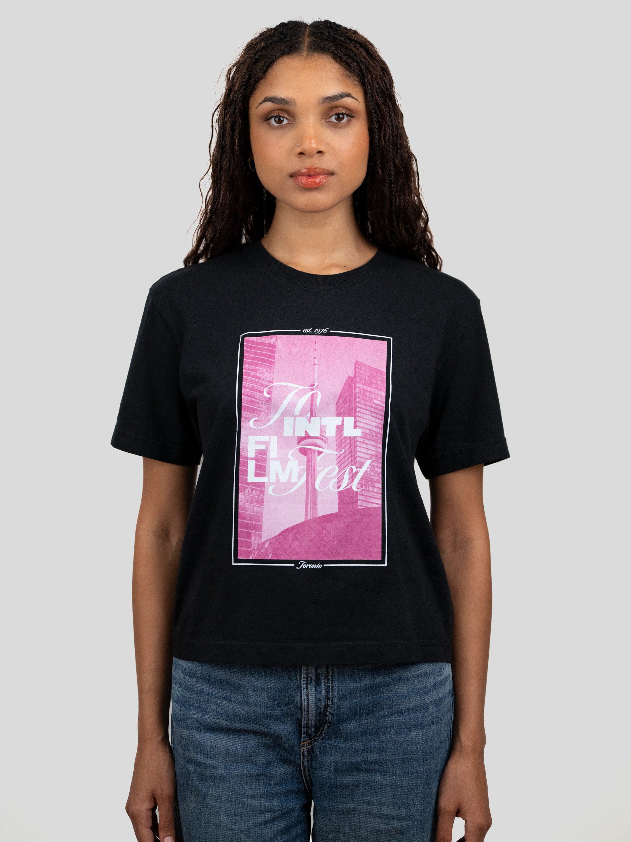 A woman wearing a black graphic t-shirt with a pink and white print, paired with blue jeans, against a solid gray background.