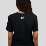 A person shown from the back wearing a black short-sleeve T-shirt with a small white 'tiff' logo centered on the upper back, paired with blue jeans against a light gray studio background.
