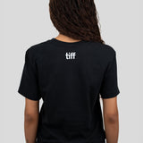 A person shown from the back wearing a black short-sleeve T-shirt with a small white 'tiff' logo centered on the upper back, paired with blue jeans against a light gray studio background.