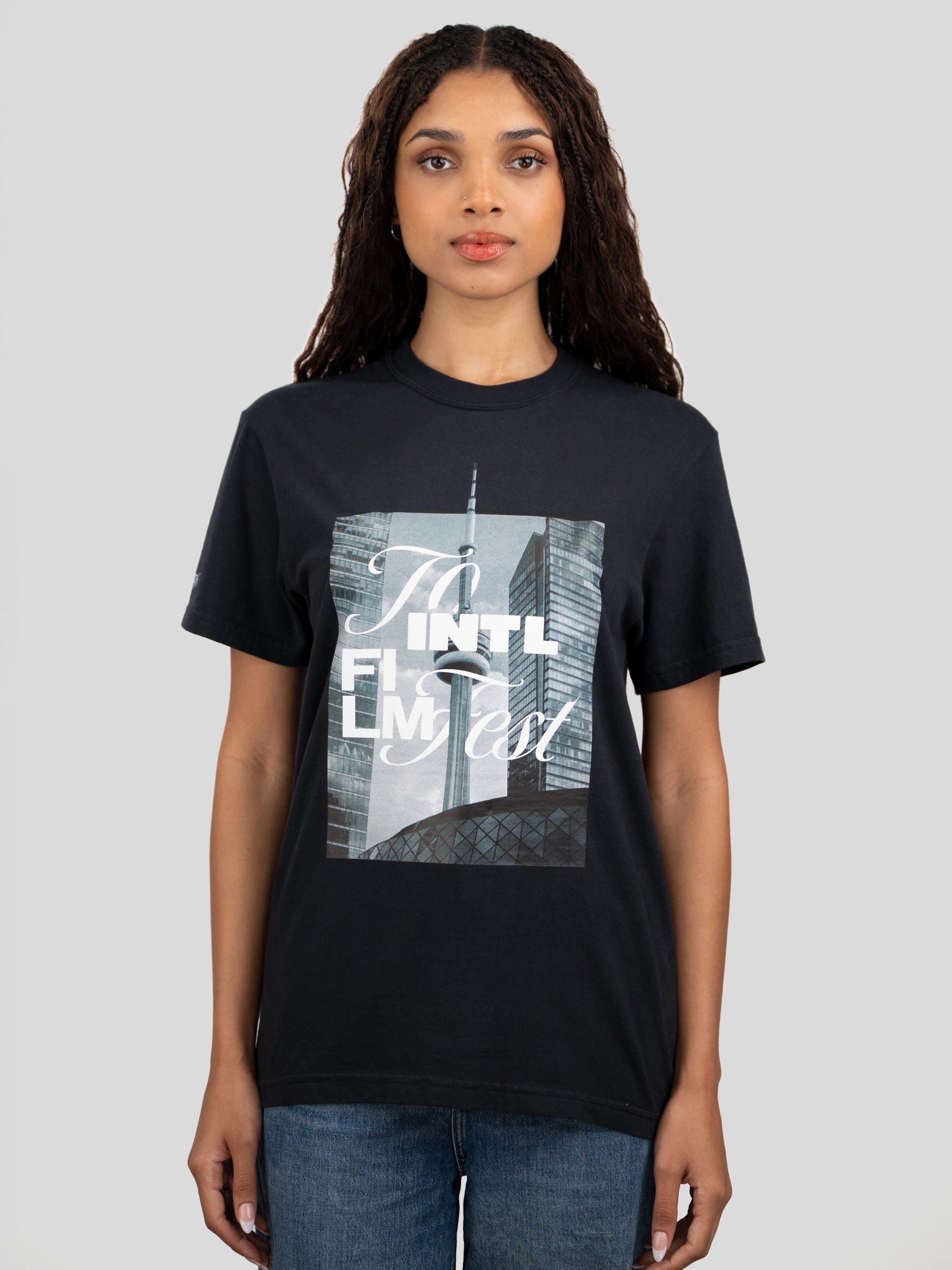 A woman modeling a black short-sleeve graphic t-shirt with a rectangular print of the New York City skyline featuring the text 'TO INTL FILM FEST'.