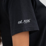 The sleeve of a t-shirt that reads est. 1976.