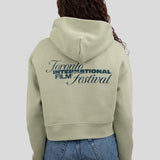 A model viewed from behind wearing a light sage green cropped hoodie with a dark green graphic print reading 'Toronto International Film Festival' on the back, paired with blue jeans against a solid gray background.