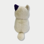 Back view of off-white cat plush toy with a distinct purple patch on its left ear against a plain light background.


