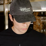 A man wearing a black t-shirt with a 'Toronto International Film Festival' graphic and a matching black baseball cap, standing in a bar environment.