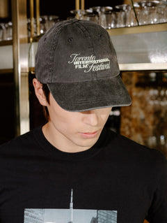 A man wearing a black t-shirt with a 'Toronto International Film Festival' graphic and a matching black baseball cap, standing in a bar environment.