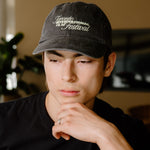 A man wearing a black t-shirt with a 'Toronto International Film Festival' graphic and a matching black baseball cap, standing in a bar environment.