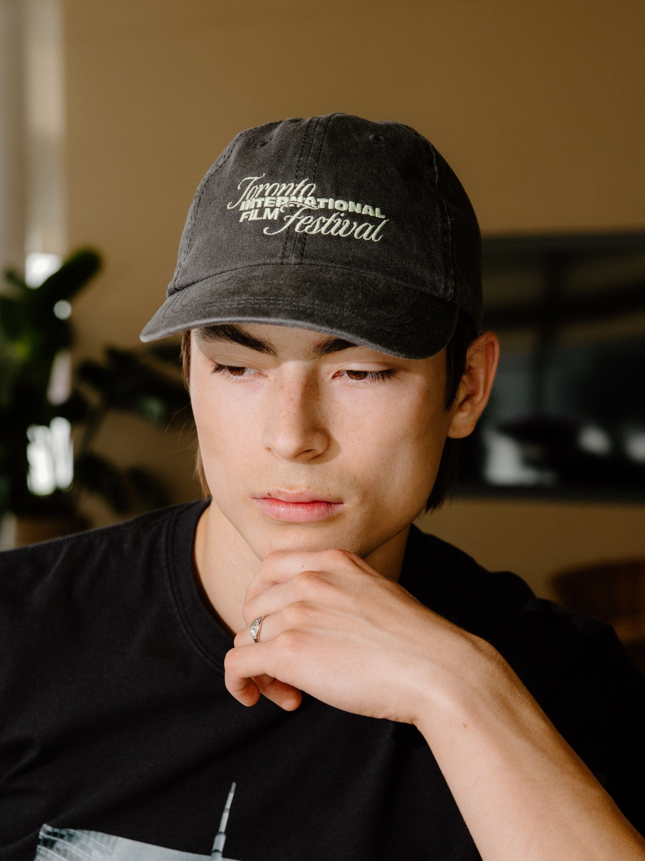A man wearing a black t-shirt with a 'Toronto International Film Festival' graphic and a matching black baseball cap, standing in a bar environment.