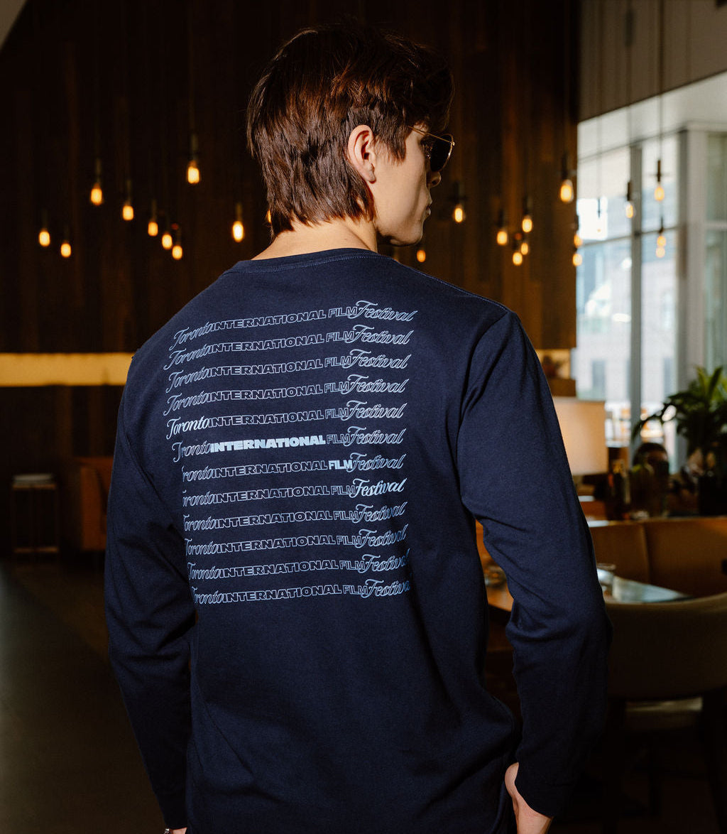 A man wearing a navy blue long-sleeve shirt with a white graphic print on the back, photographed from behind in a dimly lit indoor environment.