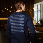 A man wearing a navy blue long-sleeve shirt with a white graphic print on the back, photographed from behind in a dimly lit indoor environment.