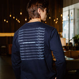 A man wearing a navy blue long-sleeve shirt with a white graphic print on the back, photographed from behind in a dimly lit indoor environment.
