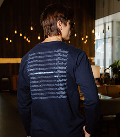 A man wearing a navy blue long-sleeve shirt with a white graphic print on the back, photographed from behind in a dimly lit indoor environment.